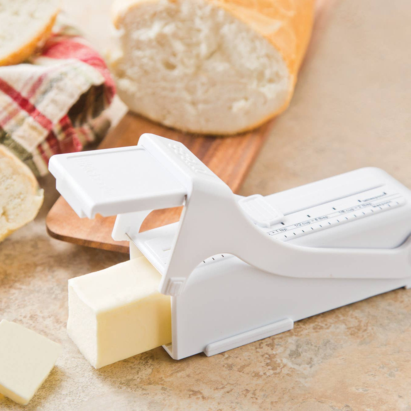 Butter slicer with butter slices on a wooden cutting board with bread in the background
