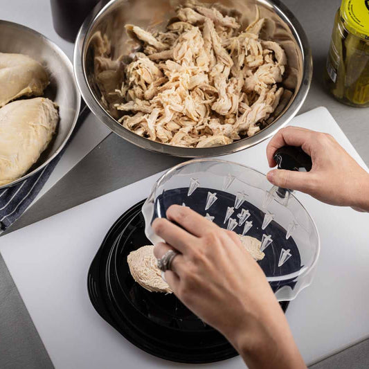 Person preparing chicken breasts on a kitchen counter with various ingredients and utensils.