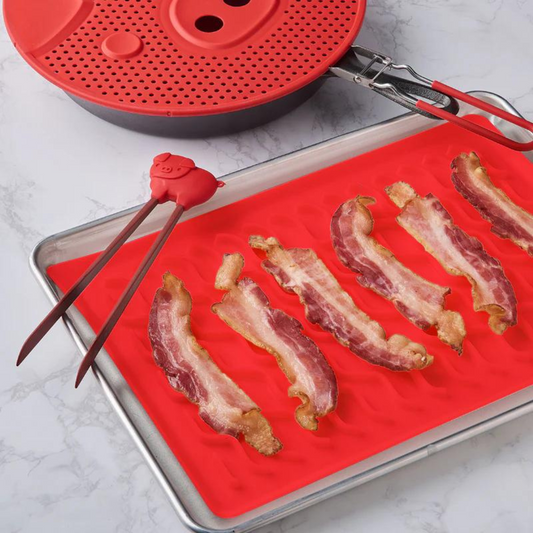 Red Oven Bacon Mat with bacon and tongs on a white table.