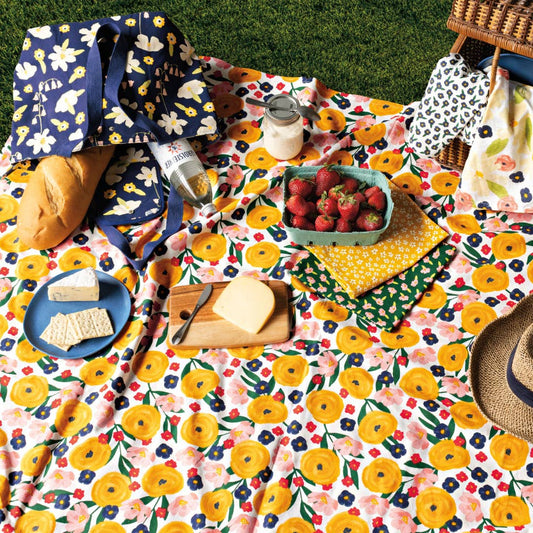 Floral-patterned picnic blanket with food and picnic items on a grassy surface