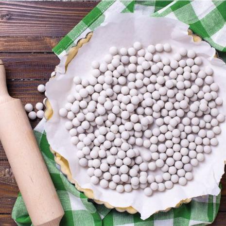 Mrs. Anderson's Ceramic Pie Weights keep empty pie shells from shrinking, bubbling, and buckling during the blind baking process in a pie dough on a table
