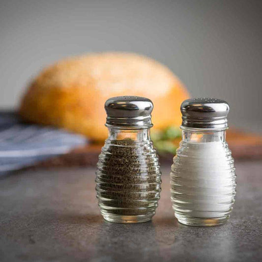 Two salt and pepper shakers on a kitchen counter with bread in the background.