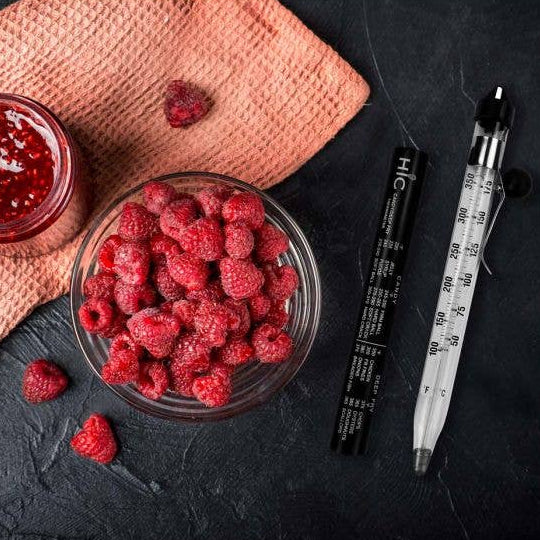 Bowl of raspberries next to a jar of raspberry jam on a dark surface with a pink cloth.