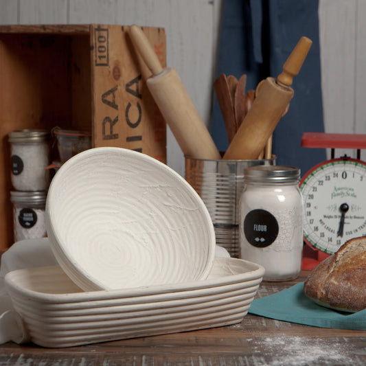Bread basket and loaves of bread on a wooden table with kitchen utensils and ingredients in the background.
