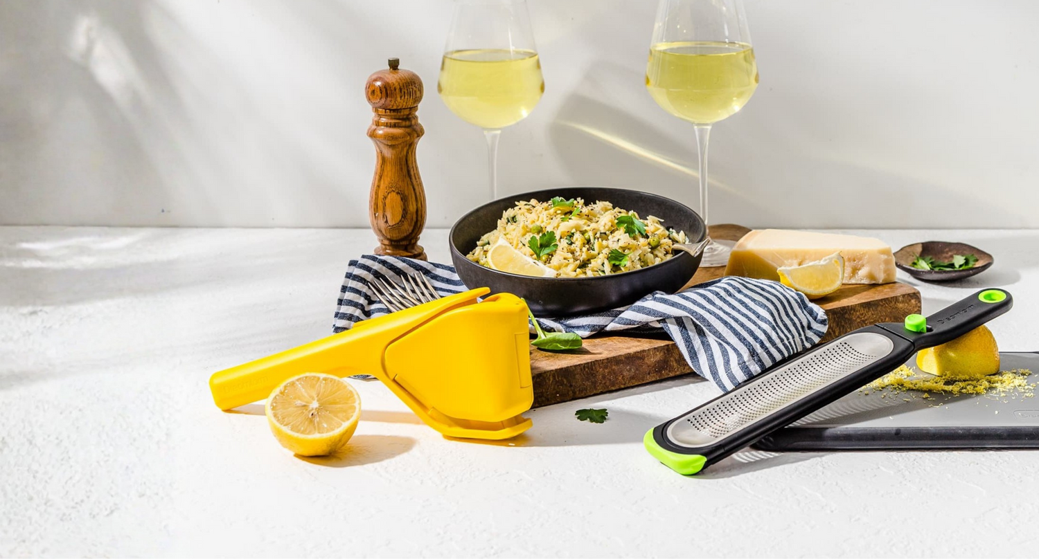 Table setting with a pan of food, lemons, and kitchen tools on a white surface.