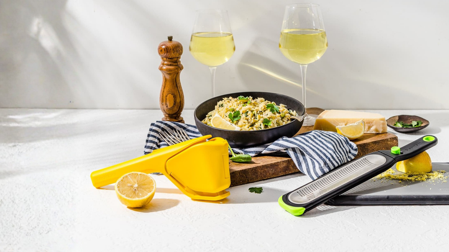 Table setting with a pan of food, lemons, and kitchen tools on a white surface.