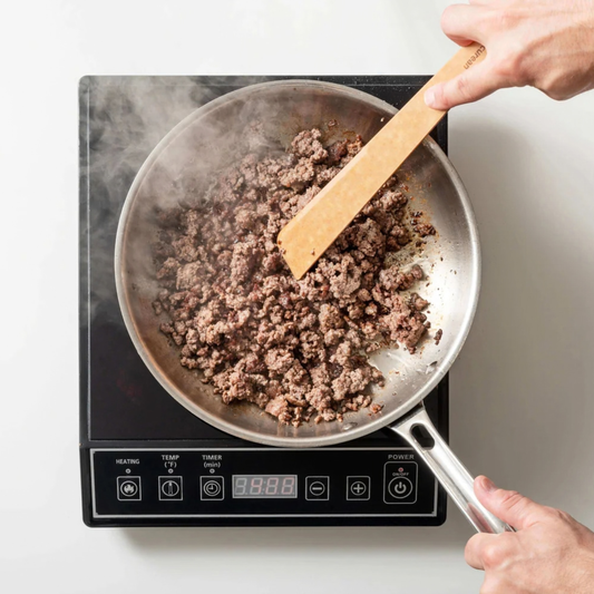 Person stirring ground meat in a frying pan on an induction cooktop.