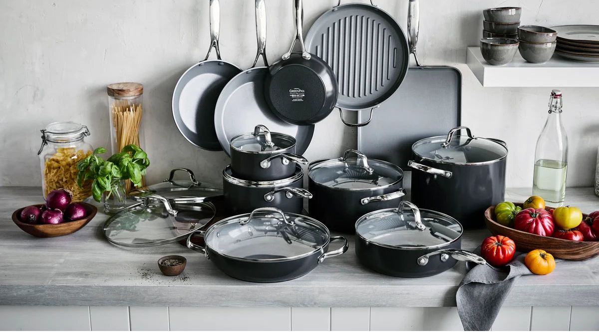 Set of cookware including pots, pans, and lids on a kitchen counter with ingredients.