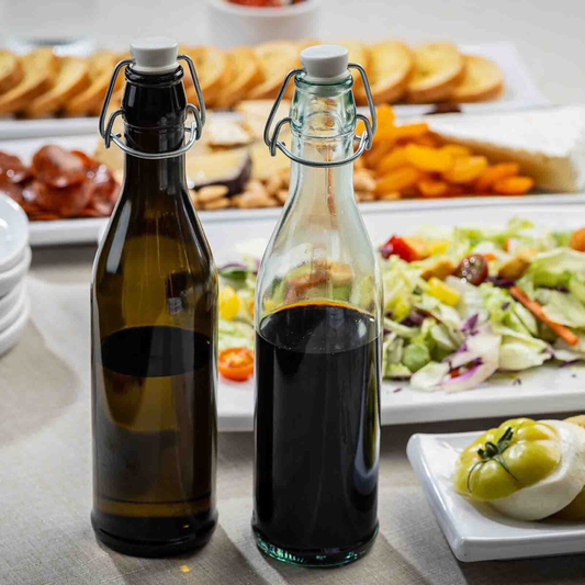 Two bottles of dark liquid on a table with food in the background