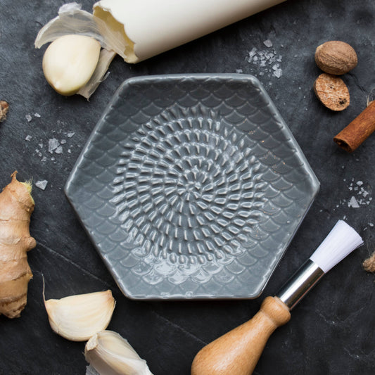 The Grate Plate is a ceramic grating plate used to grate garlic, ginger, peppers, nutmeg, chocolate, hard cheeses and much more! Perfect for adding fresh flavor to any dish. It's easy to clean and can be reused for an endless variety of culinary creations. Plus, the handy silicone garlic peeler and gathering brush make prepping fast and mess-free!