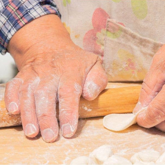 Hands rolling dough with a wooden rolling pin on a floured surface.