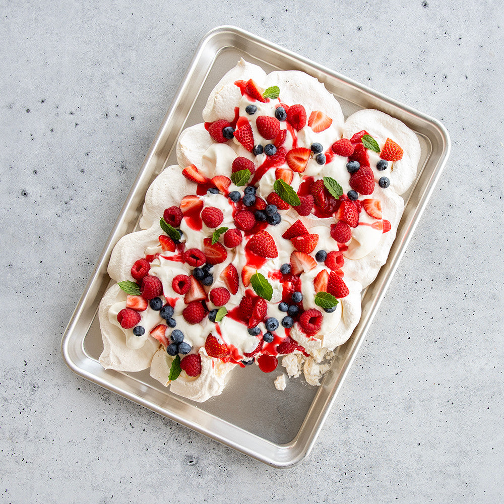 Meringue dessert with fresh berries on a metal tray against a gray background