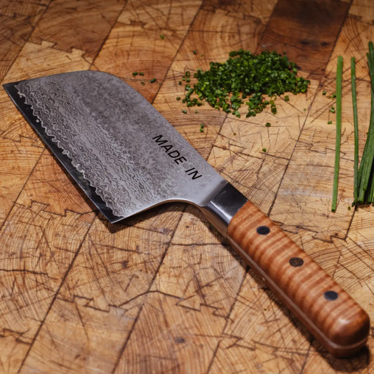 Kitchen knife with wooden handle on a wooden cutting board with chopped herbs.