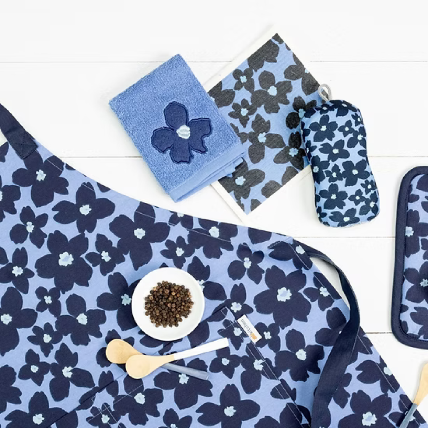 Navy floral tablecloth with matching oven mitt, towel, and hot pad on a white wooden surface.