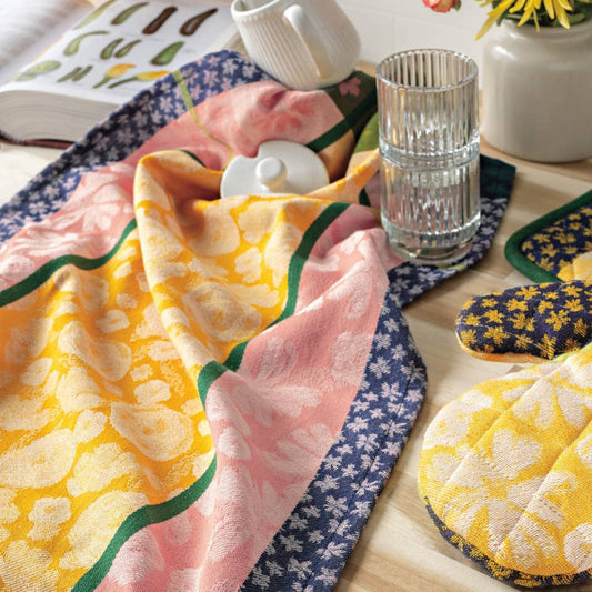 Colorful table setting with floral tablecloth, coasters, and a glass on a wooden table.