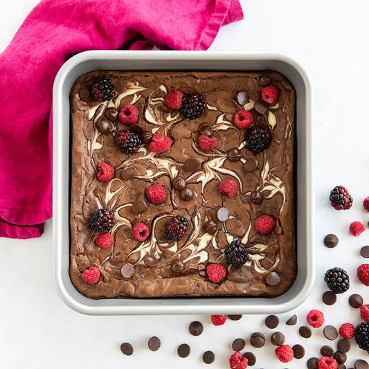 Brownie with berries and chocolate chips in a baking dish on a white background