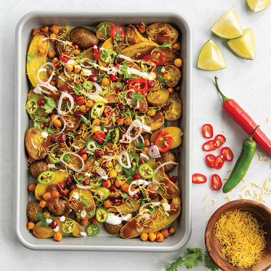 Tray of colorful roasted potatoes with various toppings on a white surface with limes and peppers.