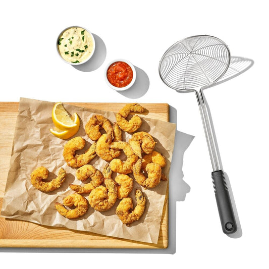 Fried shrimp on a wooden board with a strainer and sauces on a white background
