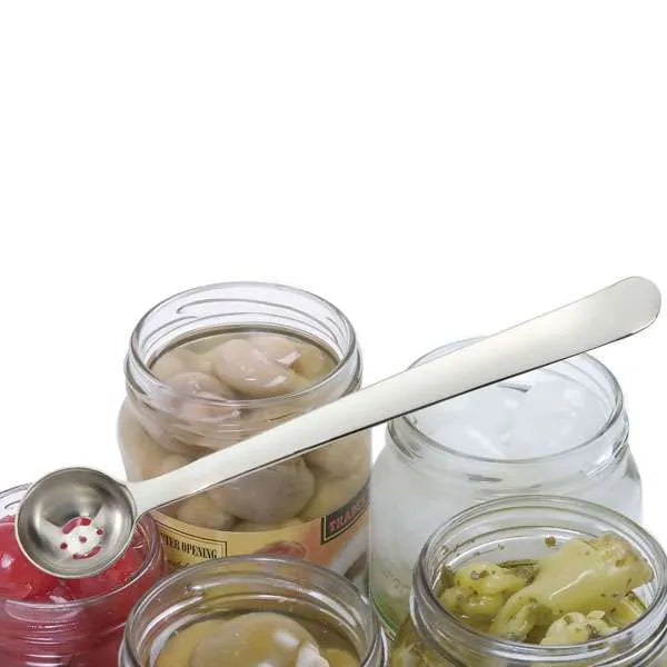 A stainless steel olive spoon with a long handle, resting across several clear glass jars containing olives on a white background.