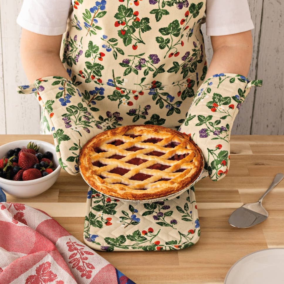 Person wearing a floral apron holding a pie, with a kitchen setting in the background.