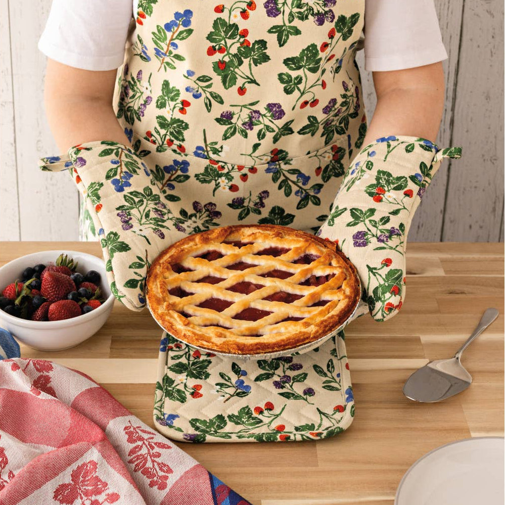 Person wearing a floral apron holding a pie, with a kitchen setting in the background.