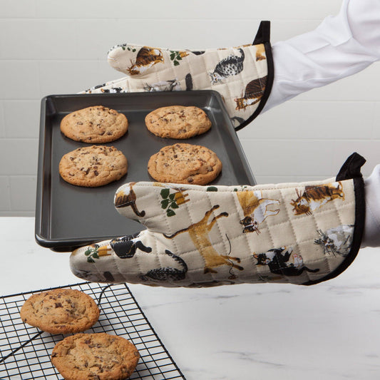 Person wearing animal-patterned oven mitts with a tray of cookies on a baking sheet.