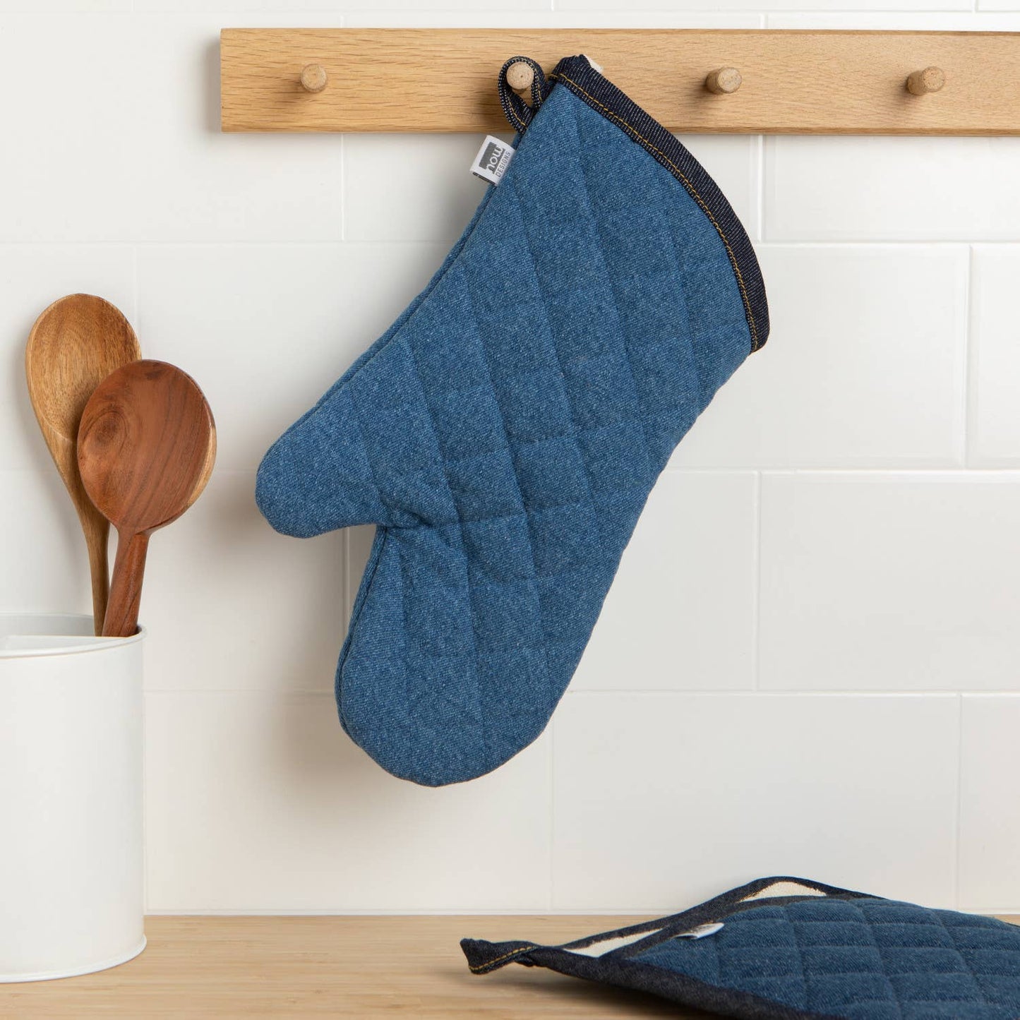 Blue oven mitt hanging on a wooden rack with kitchen utensils in the background.