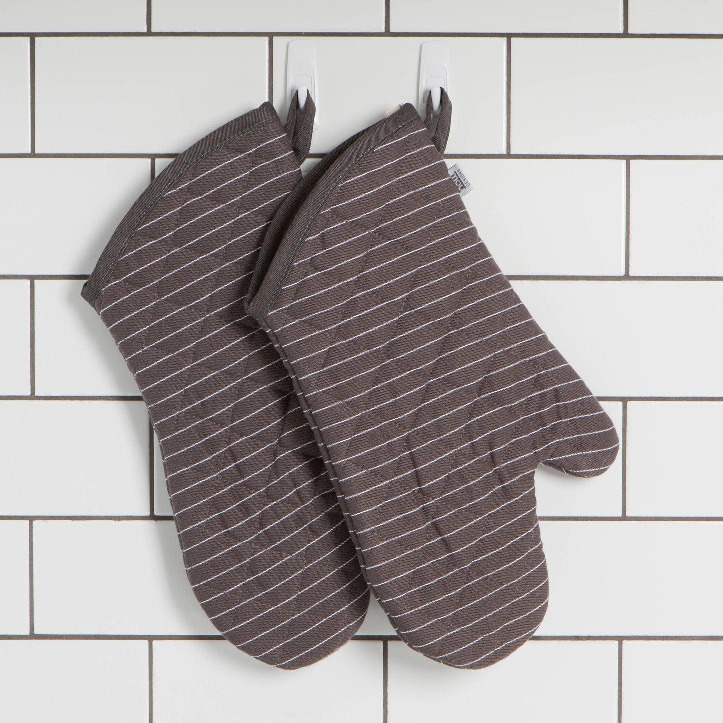 Pair of brown striped oven mitts on a white tiled wall background
