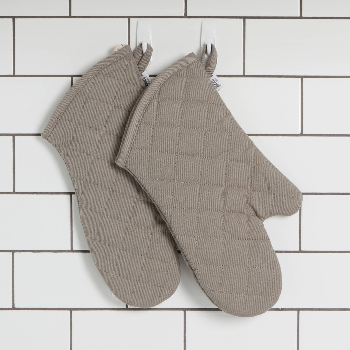 Pair of grey quilted oven mitts on a white tiled wall background