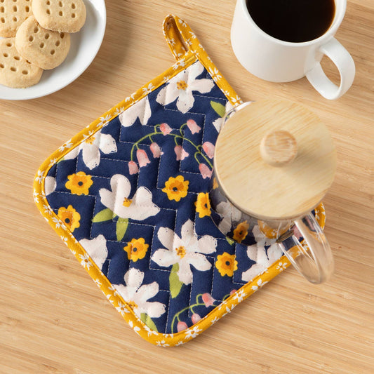 Floral hot pad on a wooden table with a cup of coffee and cookies.