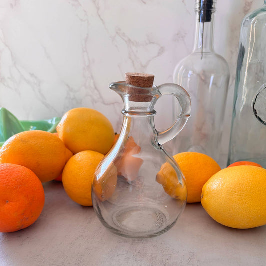Clear glass carafe with cork stopper on a surface with oranges and lemons.