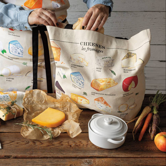 Two tote bags with cheese illustrations on a wooden table with cheese and packaging.