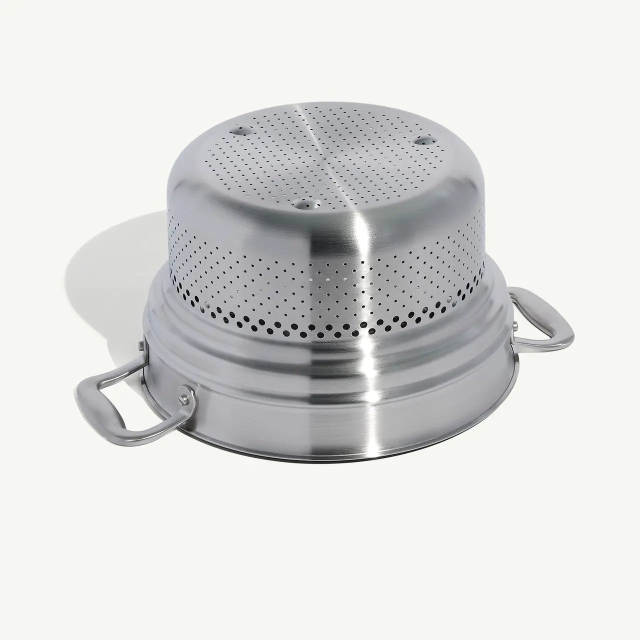 A stainless steel pasta insert with slotted holes designed to fit into a stock pot for cooking pasta on a white background.