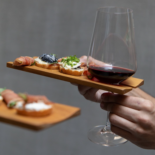 Wine glass with appetizers on a wooden plate with a gray background