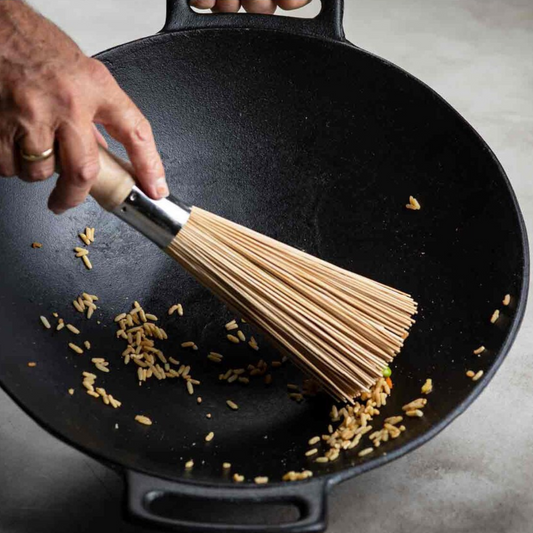 Wok wisk brusing rice out of a black wok on a gray background