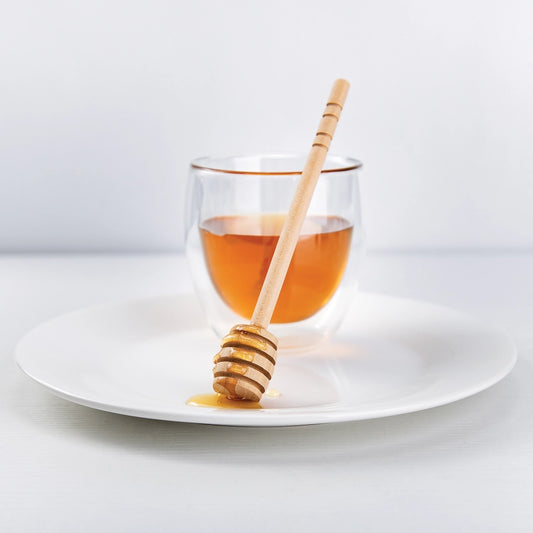 Wooden honey dipper with cup of honey on a white plate with a white background