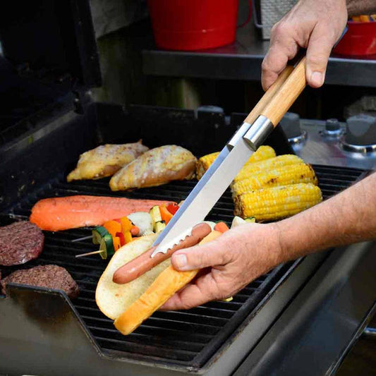 Person grilling hot dogs and vegetables on a barbecue with a basting brush.