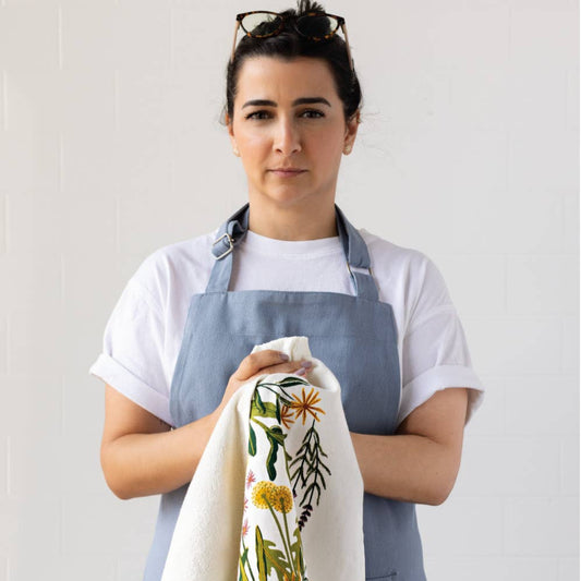Woman wearing a blue apron holding a floral towel against a white background