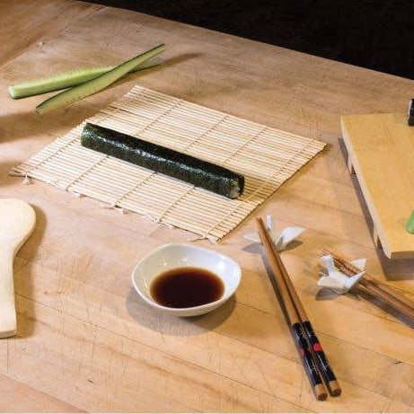 Sushi preparation setup on a wooden table with sushi rolls, soy sauce, and chopsticks.