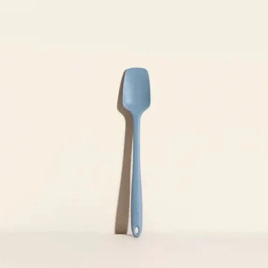 A slate blue spoonula with a curved bowl and a handle, designed to reach into tall, thin jars.