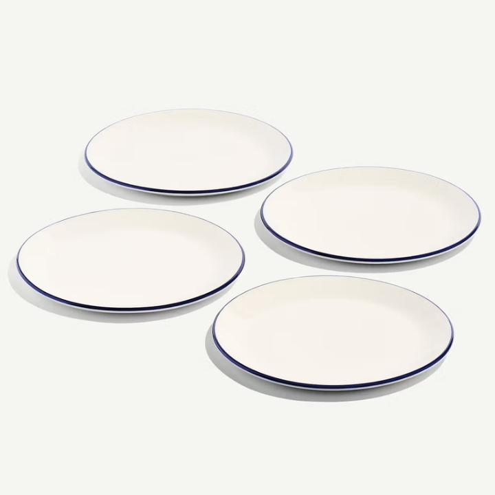 Four white oval plates with a thin dark blue rim, arranged on a light off-white background.