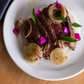 Plated dish of sliced meat with onions and garnishes on a white plate.