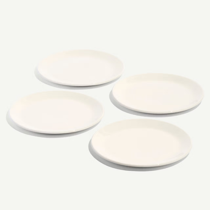 Four round white ceramic plates arranged in a loose square on a clean white background.
