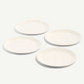 Four round white ceramic plates arranged in a loose square on a clean white background.