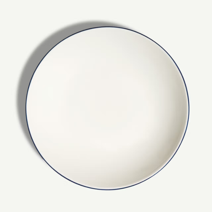 A top-down view of a round white ceramic plate with a thin dark blue rim, set against a clean off-white background with a soft shadow.