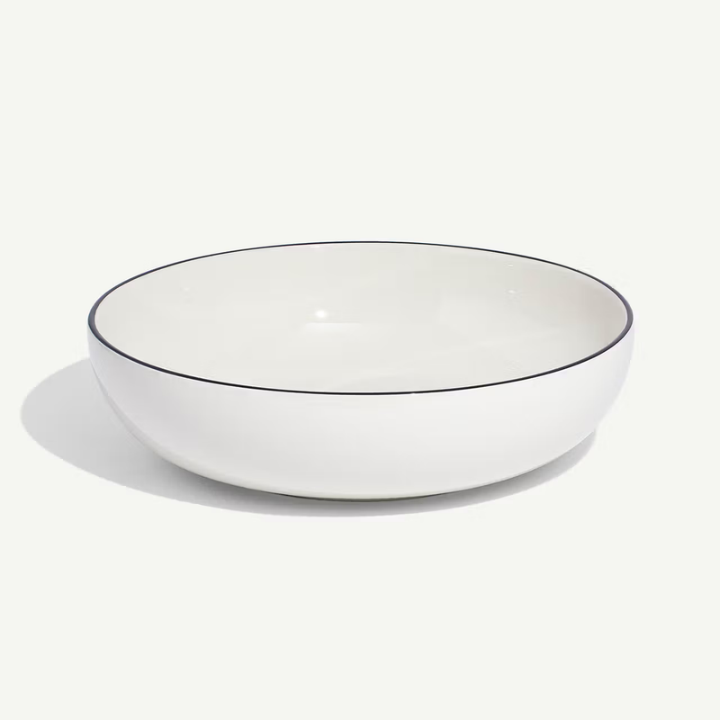 A white ceramic bowl with a thin black rim, photographed on a clean off-white background with a soft shadow.