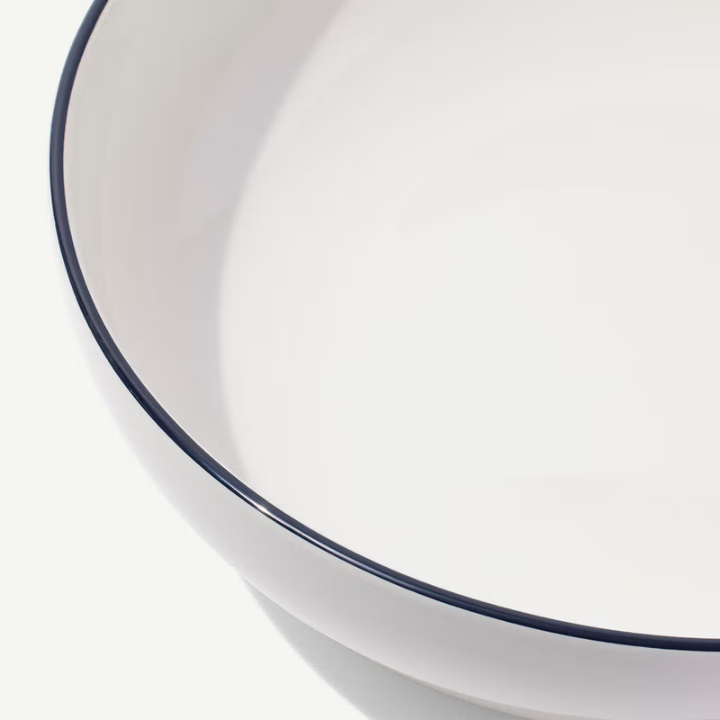 Close-up of a white ceramic bowl with a thin dark navy blue rim, shown against a clean white background.