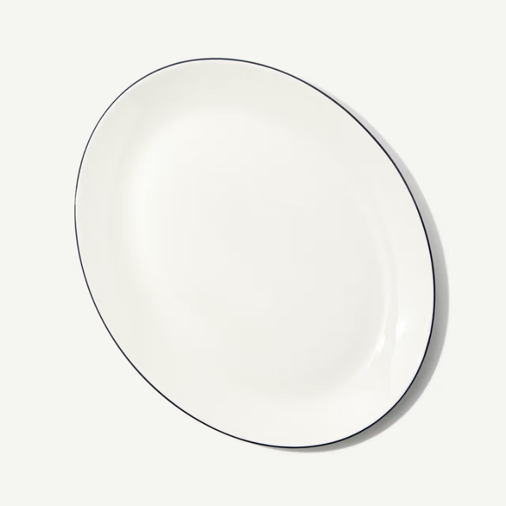 An oval white ceramic serving platter with a thin black rim, photographed from an overhead angle on a clean white background.