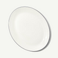 An oval white ceramic serving platter with a thin black rim, photographed from an overhead angle on a clean white background.