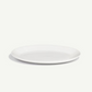 A minimalist white ceramic plate with a shallow rim, photographed from a high angle on a clean, off-white background with a soft shadow.